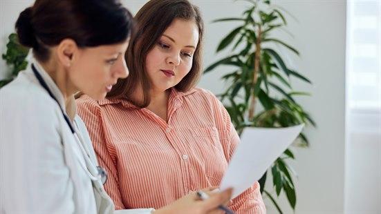 Illustrasjonsfotoet viser en overvektig kvinne sammen med helsepersonell. De går gjennom et ark sammen. 