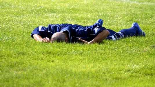 En fotballspiller ligger med kroppen ned mot gresset