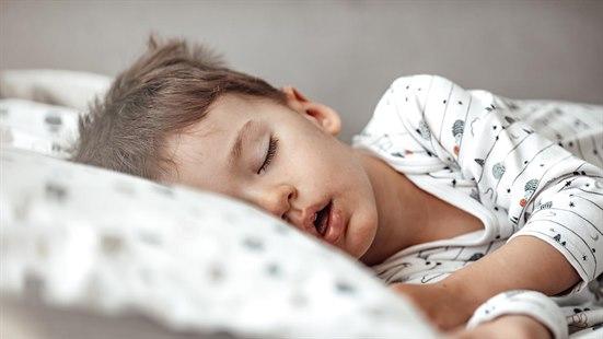Illustrasjonsfoto av en liten gutt som sover fredelig i sengen. Ansiktet ligger avslappet mot hodeputen og han sover med munnen åpen.