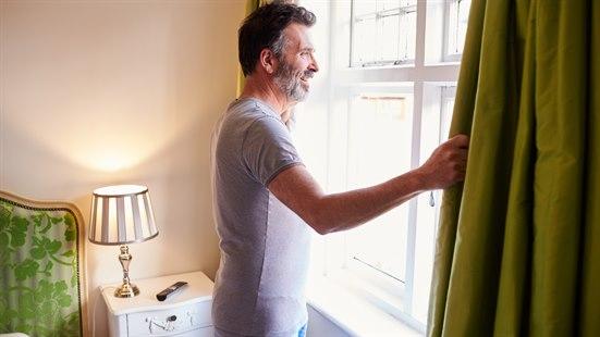 Illustrasjonsfoto at en mann som står på soverommet om morgenen og ser ut vinduet.