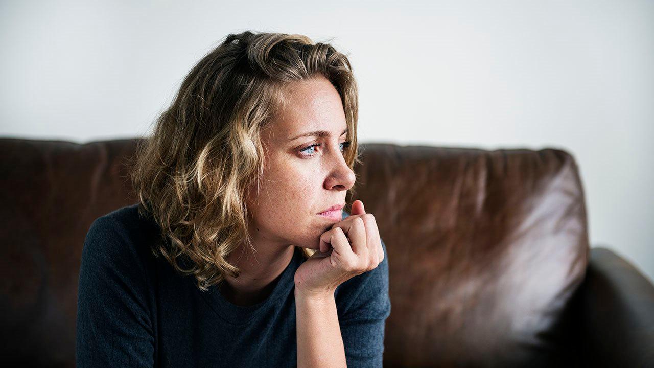 Illustrasjonsfoto av bekymret kvinne som sitter i en sofa. Hun støtter hode med hånda på haken og ser mot høyre side.