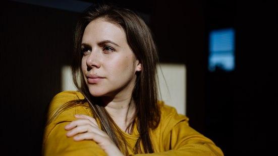 Illustrasjonsfoto av kvinne i med langt mørkt hår og gul genser med tankefullt uttrykk. Mørke omgivelser.