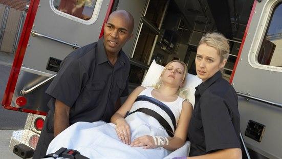 Illustrasjonsfoto av to ambulansearbeidere som løfter en pasient i en bære båre ut av ambulansen