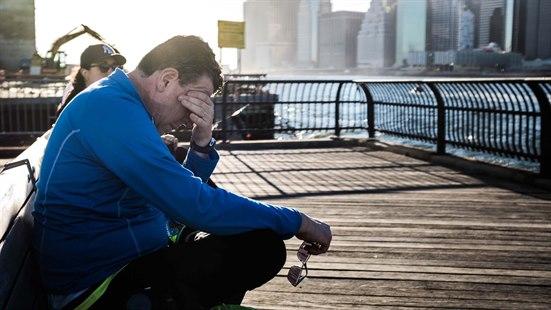 Sliten mann sitter på en brygge og lener hode mot hånden. I bakgrunnen ser vi en storby.