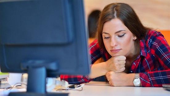 Illustrasjonsfoto av en kvinne som er sliten og sitter foran en pc. Hun hviler haka på hendene. 