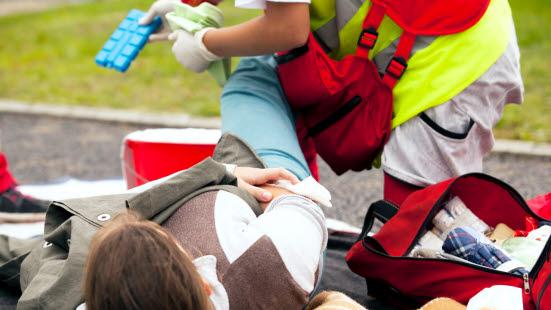 Liggende pasient utendørs får foten undersøkt av Ambulansearbeider for blødning