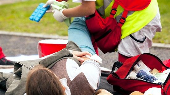 Liggende pasient utendørs får foten undersøkt av Ambulansearbeider for blødning