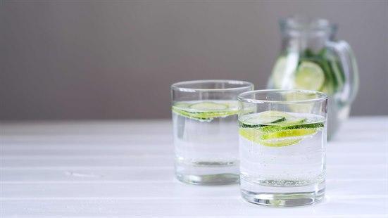 Illustrasjonsfoto: To vannglass med agurk- og sitronskiver står på et bord. Vannmugge i bakgrunnen.