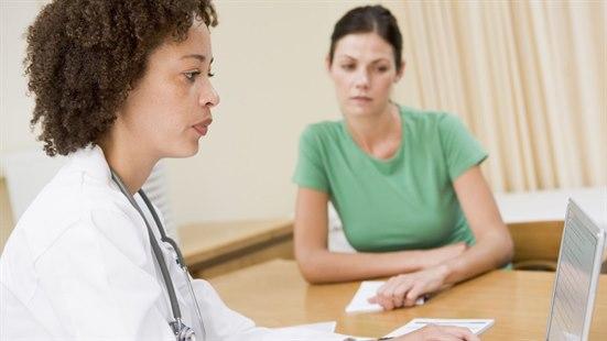 Illustrasjonsfotoet viser en kvinnelige lege som ser mot sin dataskjerm. Ved siden av sitter en kvinnelig pasient