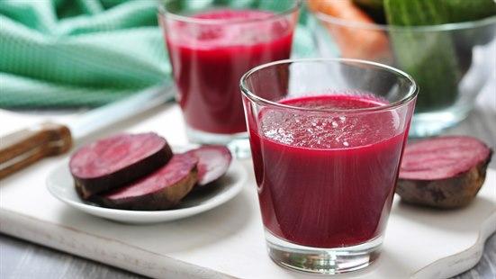 Illustrasjonsfoto av et et glass rødbetejuice med oppskåret rødbeter liggende ved siden.