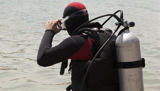 Illustrasjonsfoto av flaskedykker ved vannkanten, setter på seg masken.