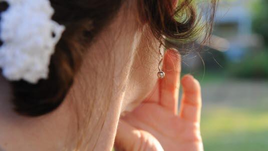 Fotoet viser den høyre nedre delen av hodet og halsen til en dame sett bakfra. Hun holder sin venstre hånd foran munnen. 