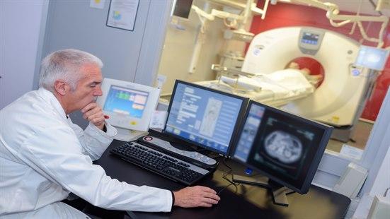 Lege ser på skjermbilder mens en pasient får utført MR-undersøkelse.