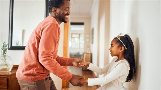 BIlde av far og datter som danser sammen hjemme i stua. 