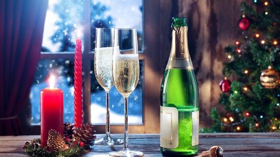Illustrasjonsbilde av ei sjampanjeflaske, med to fylte glass ved siden. På bordet er det tente julelys og et juletre står i bakgrunnen.
