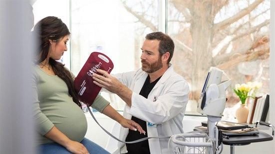 Illustrasjonsfotoet viser en mannlig lege som setter på en blodtrykksmansjett på en gravid kvinnes arm