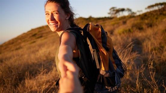 Illustrasjonsfoto av en ung, glad kvinne på tur i naturen - som rekker ut hånda og griper hånda til en annen.