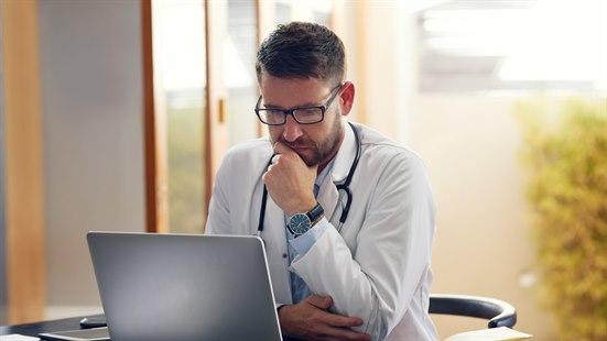 Illustrasjonsfoto viser en lege som sitter ved en pult og ser studerende på en datamaskin