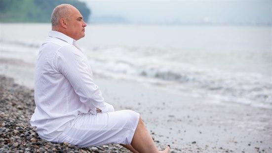 Illustrasjonsfotoet viser en voksen mann som sitter på en strand og ser utover havet