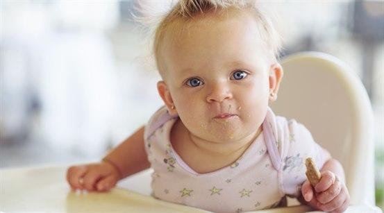 Jentebaby spiser kjeks i babystol.